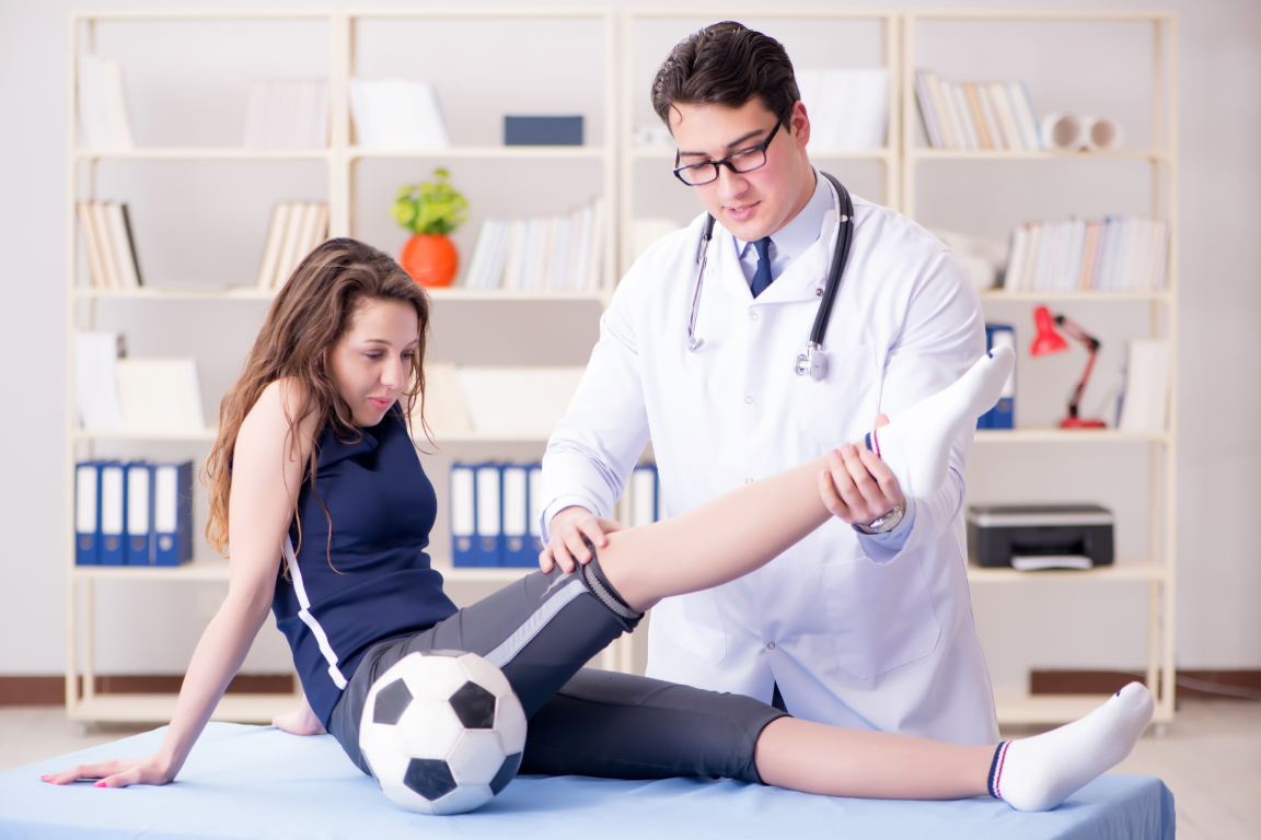 A doctor in a white coat performing a knee and leg examination on a female soccer player in a clinical setting.